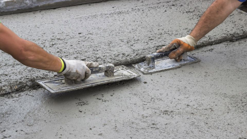This photo shows two workers hands smoothing out freshly poured concrete