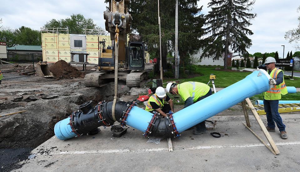 This photo shows 3 construction workers preparing a pipe to go in the ground.